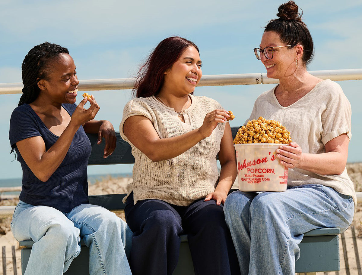 Three friends sharing a Johnson's caramel popcorn tub on the Ocean City boardwalk